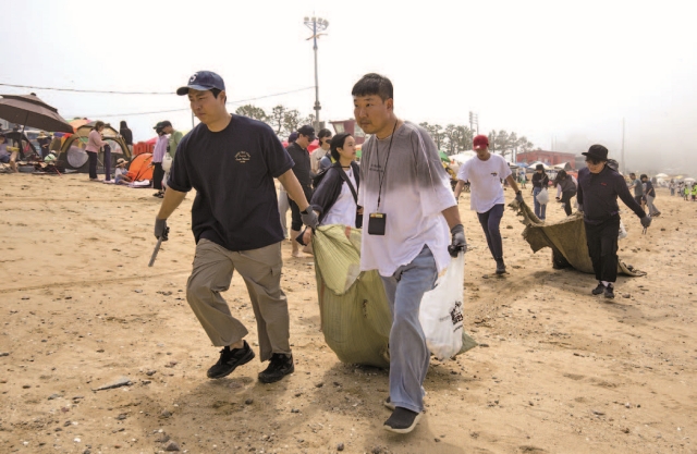 알줍캠페인 참가자들이 해변에서 주운 쓰레기를 넣은 마대자루를 끌고 있다. 