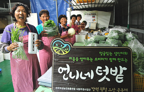 언니네텃밭 오산공동체 농민들이 꾸러미에 들어간 농작물을 들어보이며 활짝 웃고 있다. 