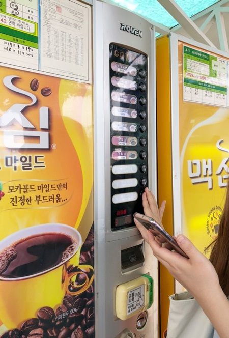 성인 여성이 똑바로 일어서서 손을 뻗어야만 음료 메뉴 버튼을 누를수 있다.