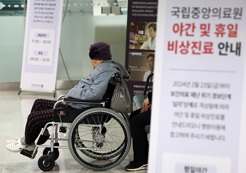 서울 중구 국립중앙의료원에 게시된 야간 및 휴일 비상진료 안내문 뒤편에서 휠체어에 앉은 환자가 진료를 기다리고 있다. (ⓒ뉴스1, 무단 전재-재배포 금지)