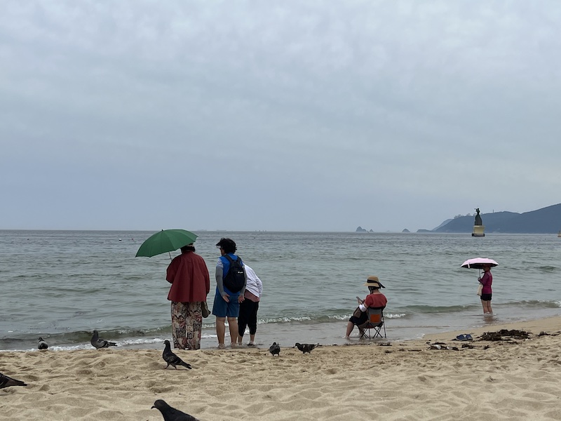 해수욕장에서 더위를 피하고 있는 사람들 모습. 양산이나 모자를 쓰고 있다.